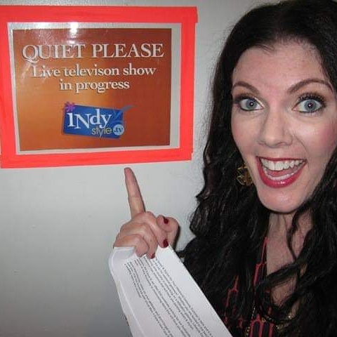 A woman pointing to the sign for an indoor television show.