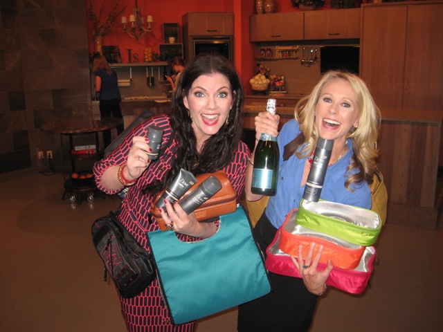 Two women holding wine and shopping bags in a room.