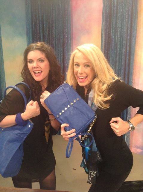 Two women holding up a blue purse and smiling.