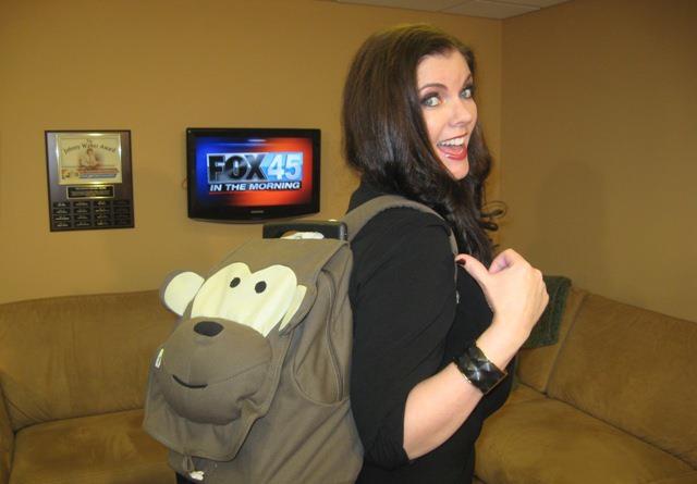 A woman with a monkey backpack in front of the television.