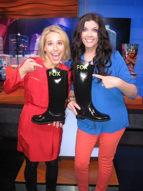 Two women holding up black boots with the word fox on them.
