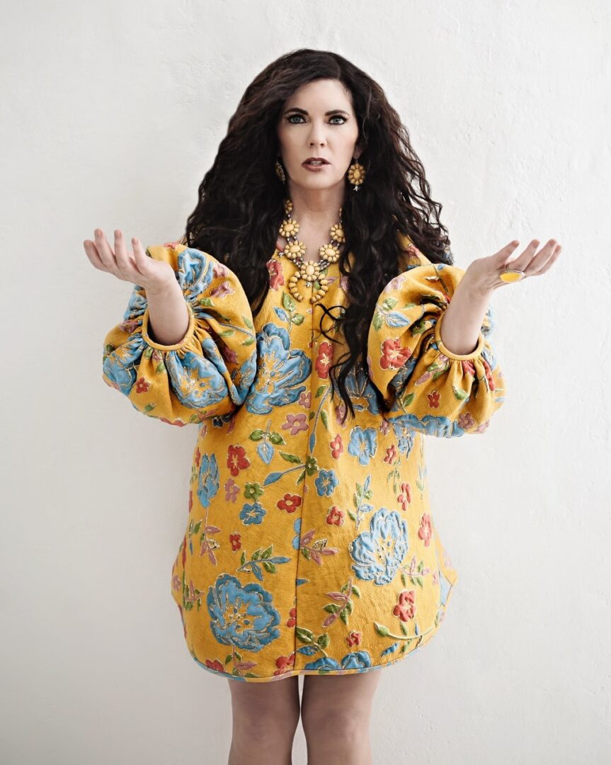A woman in a yellow floral coat shrugging.