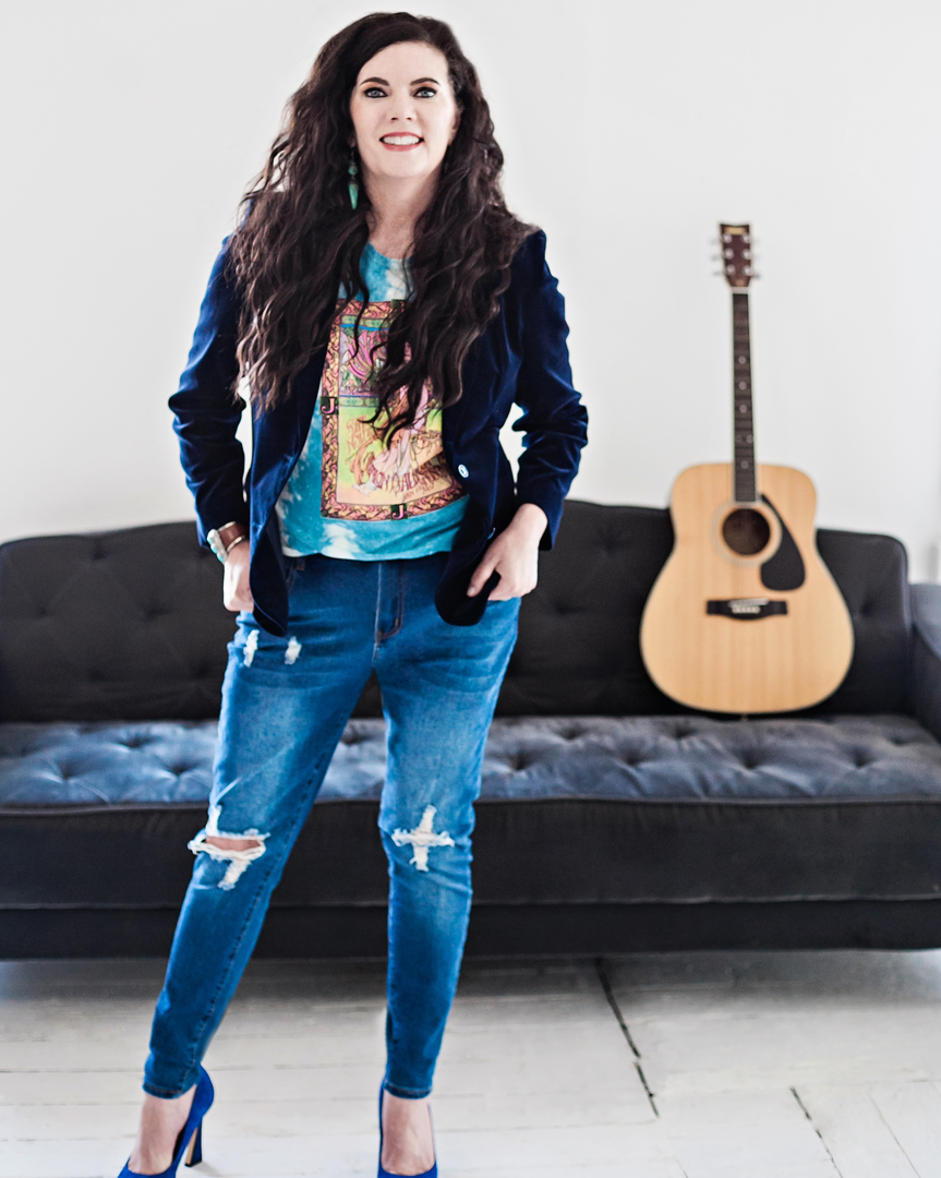 A woman standing in front of a couch with her guitar.